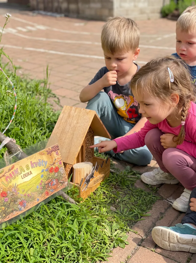 Děti prohlížejí dřevěný domeček pro hmyz na kraji záhonu